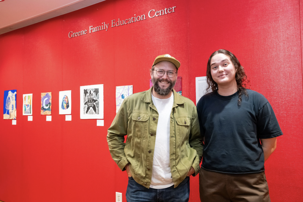 Two student artists standing in front of their artworks
