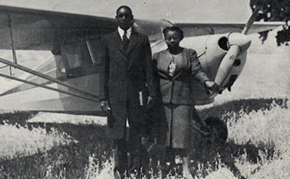 Archival photo of African American couple standing in front of an airplane