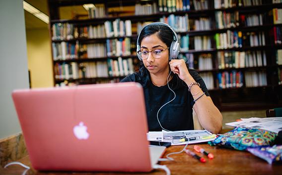 Student with headphones working at laptop in library