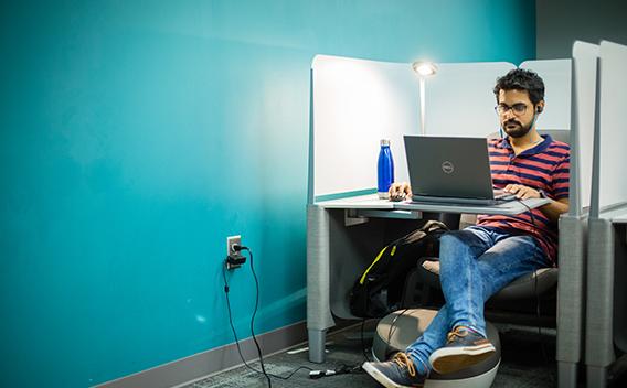 Contented student reading book on laptop in individual study cubby